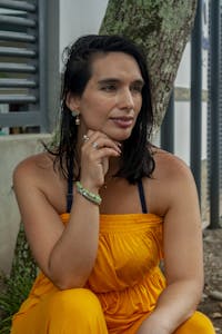 A thoughtful woman in a yellow dress sits outdoors, offering a serene summer portrait.