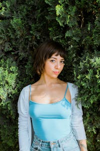 Portrait of a young woman in a blue top surrounded by lush greenery. Summer vibe.