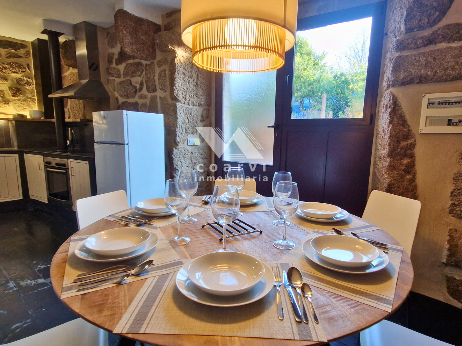 Comedor con mesa redonda y cocina al fondo en casa de Lobios