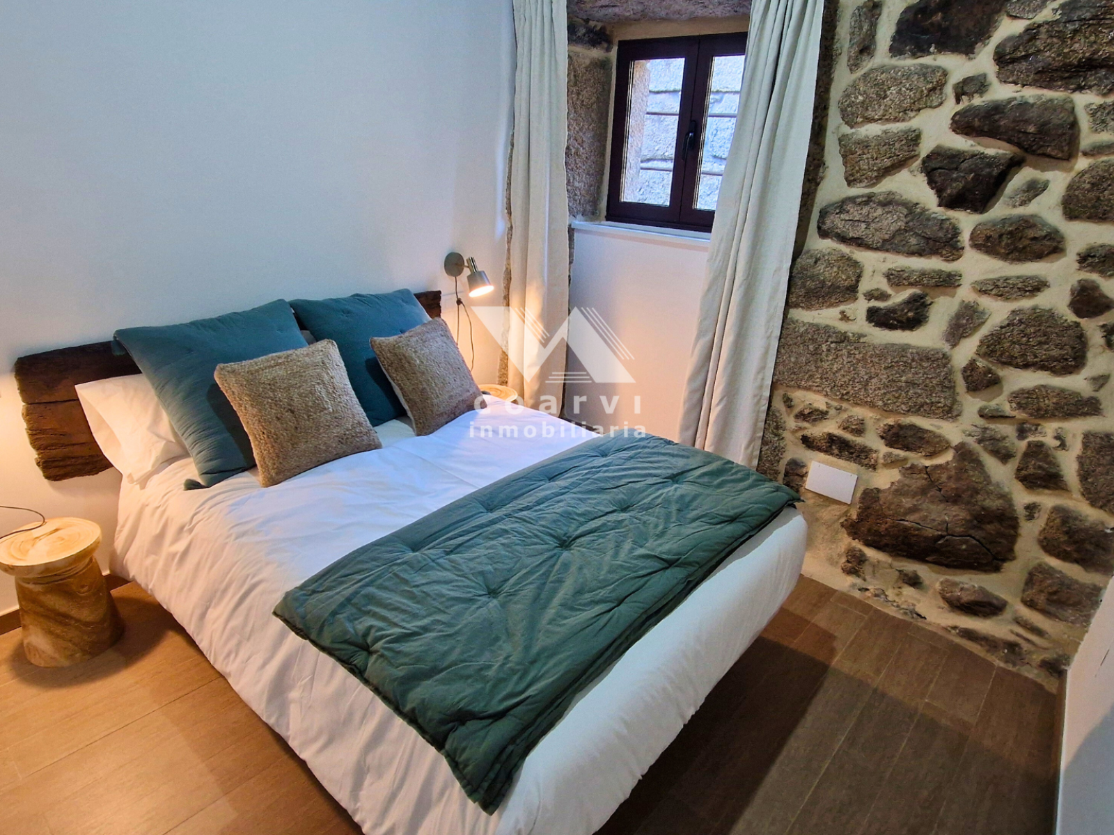 Dormitorio doble con ropa de cama verde y pared de piedra