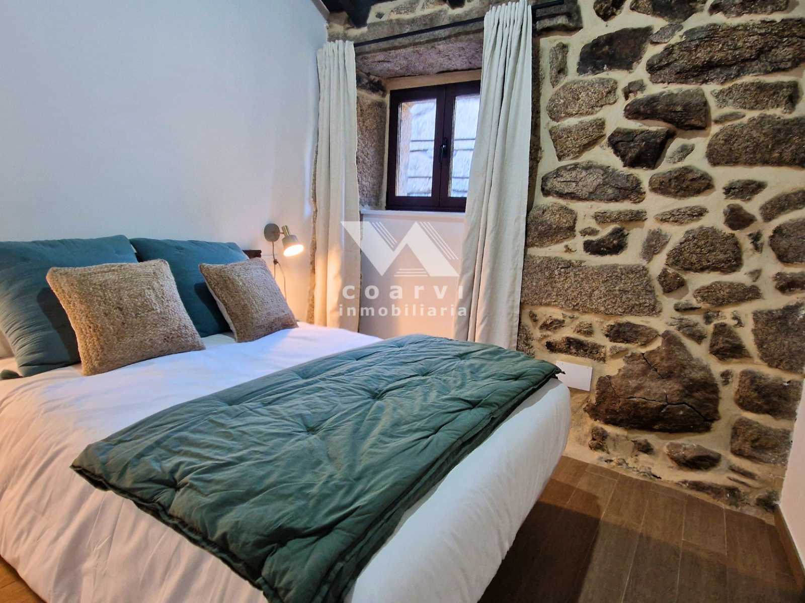 Dormitorio con cama doble y ventana en vivienda de piedra de Lobios