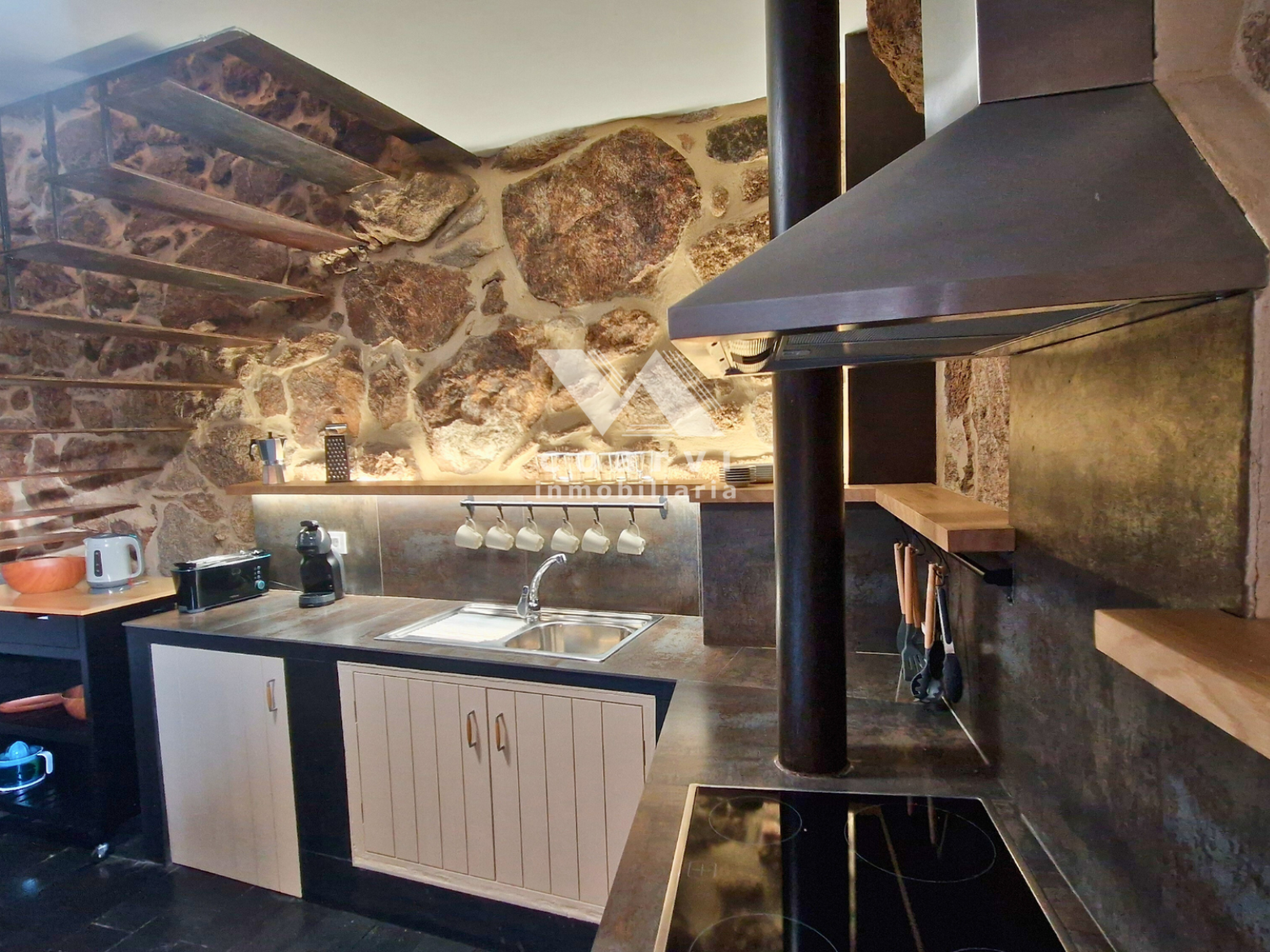 Cocina con campana extractora y encimera oscura en vivienda de Lobios