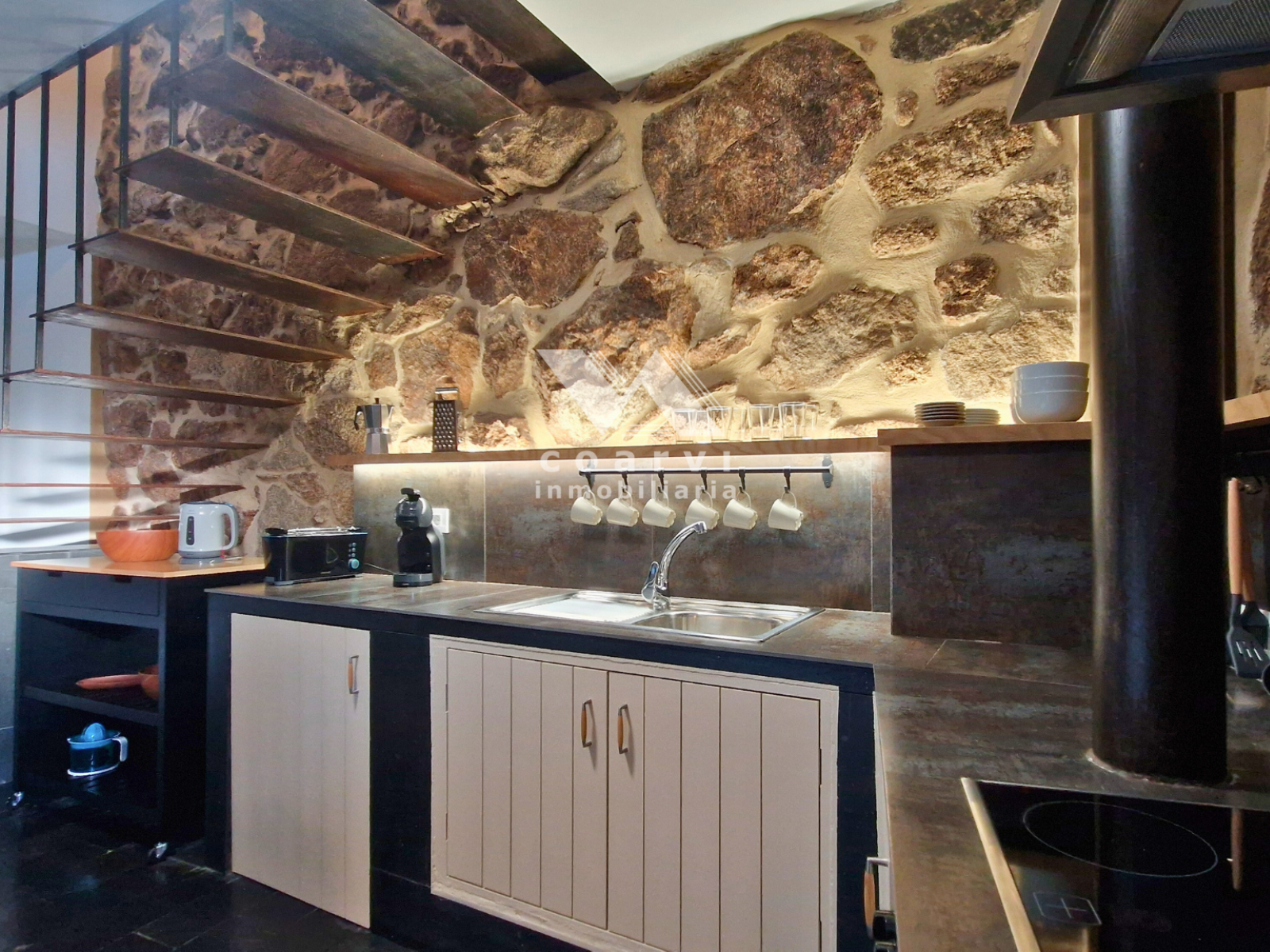 Encimera y mobiliario de cocina junto a pared de piedra vista